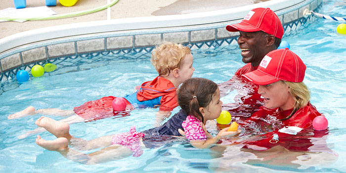 Deux sauveteurs de la Croix-Rouge assistent deux bambins dans la piscine.
