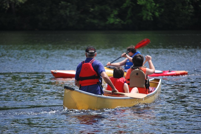 Man with two kids in a canoe, wearing lifejackets.