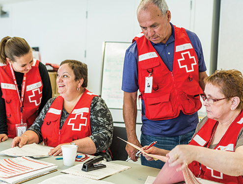 Un groupe de bénévoles de la Croix-Rouge portant des vestes, s'organisant autour d'une table.
