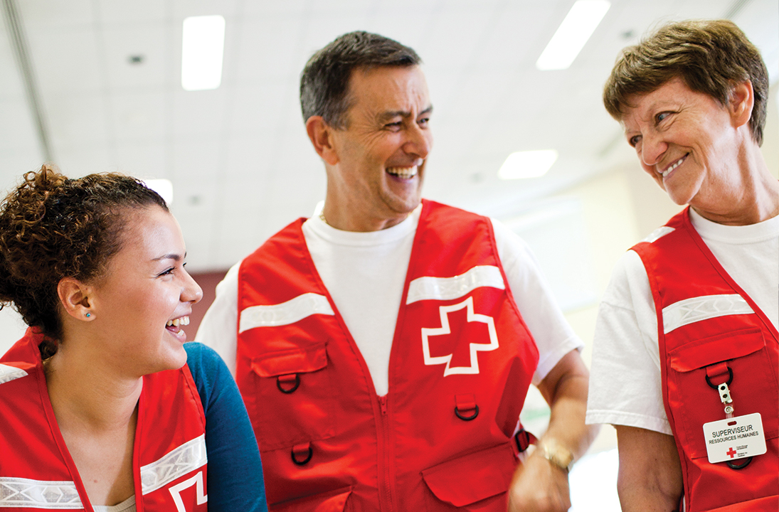 Trois volontaires de la Croix-Rouge portant un gilet rouge se sourient.