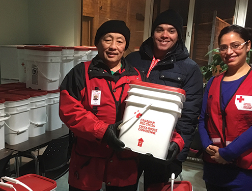 Trois bénévoles de la Croix-Rouge sourient avec un grand seau de fournitures.