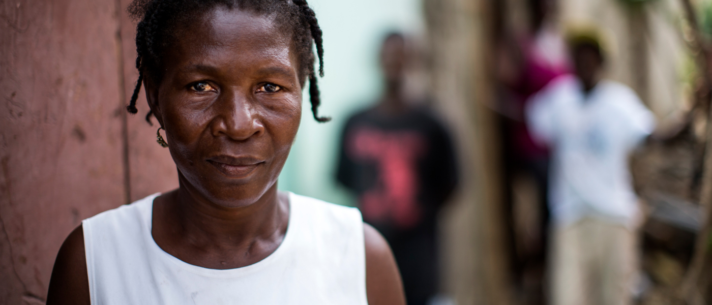 Une femme haïtienne vêtue d’un débardeur blanc regarde droit vers la caméra