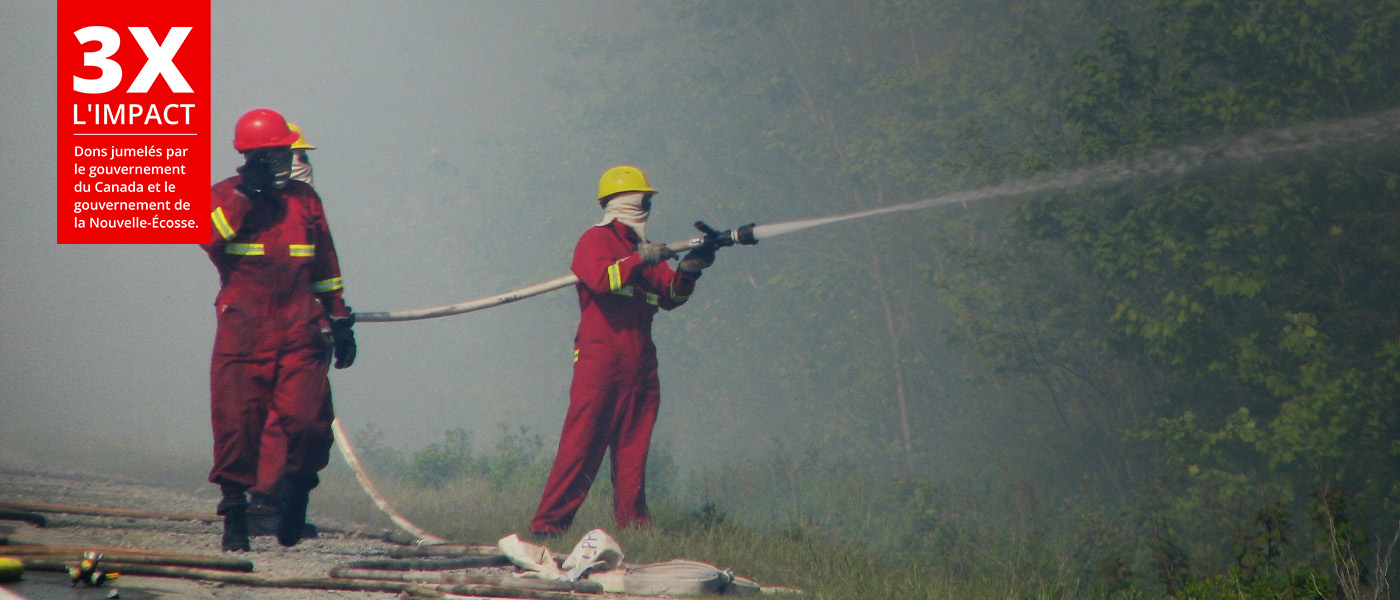 Des pompiers arrosent un feu de forêt à partir de laquelle s'élève une épaisse fumée.