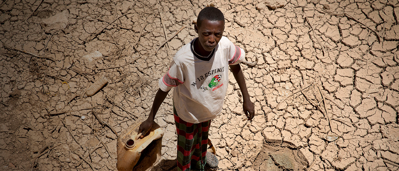 Un garçon se tient debout avec une cruche d'eau, sur le sol asséché de la Somalie.