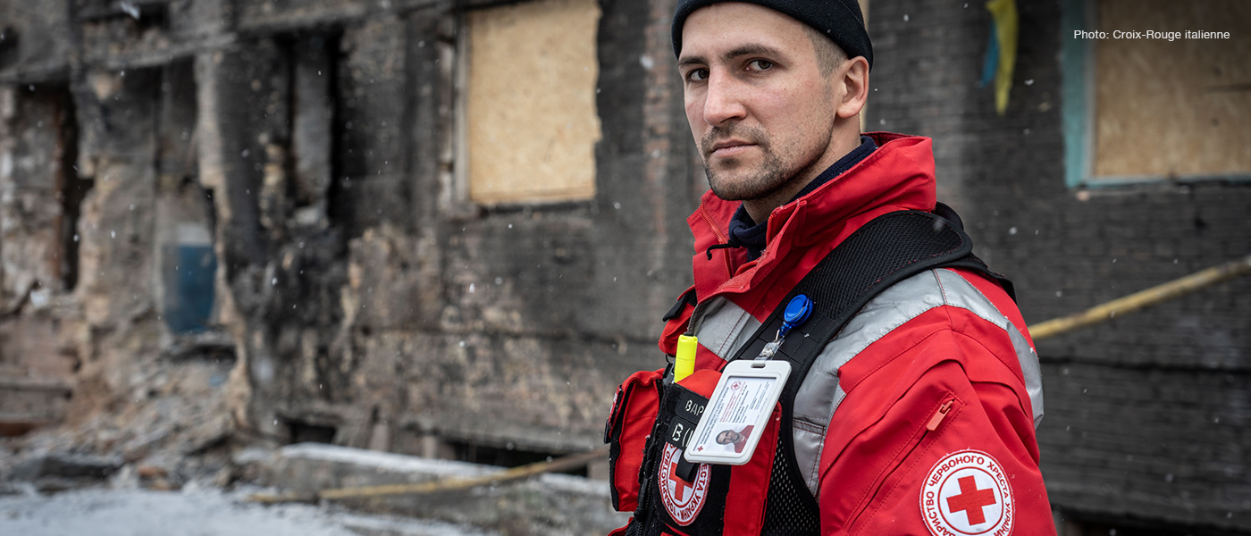 Un membre de la Croix-Rouge ukrainienne devant un édifice bombardé.