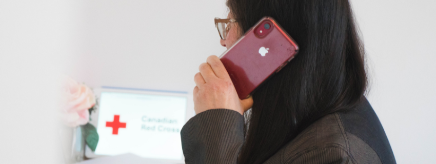 Une femme au téléphone en regardant une tablette affichant le logo de la Croix-Rouge canadienne.