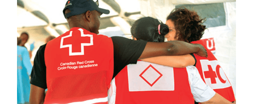 Trois bénévoles de la Croix-Rouge canadienne portant des gilets rouges s'enlacent dans une franche accolade.
