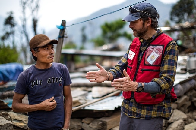 Un travailleur humanitaire de la Croix-Rouge discute avec un habitant du Népal au milieu des décombres. 