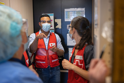 Une infirmière et un bénévole de la Croix-Rouge écoutent un homme masqué et un gilet de la Croix-Rouge