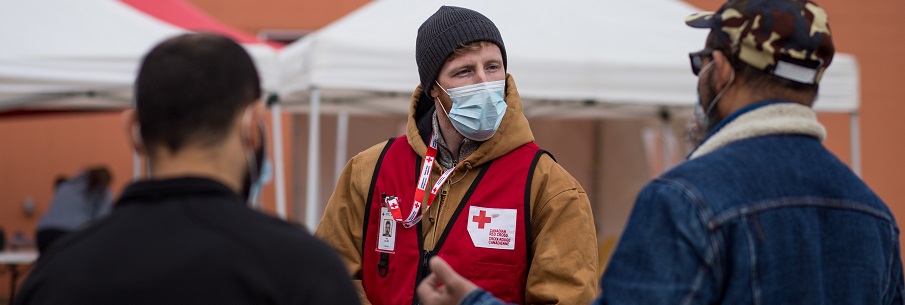 Un bénévole de la Croix-Rouge portant un masque médical parle à deux personnes