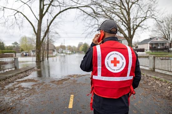 Un bénévole de la Croix-Rouge regarde une rue inondée alors qu’il est au téléphone