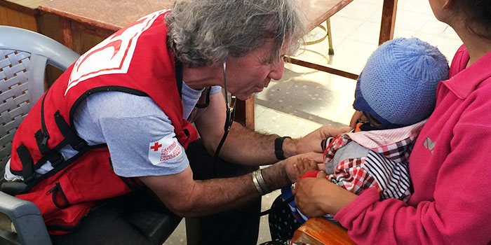 Une travailleuse du Croix Rouge prenant le pouls d’un nourrisson dans les bras de sa mère.
