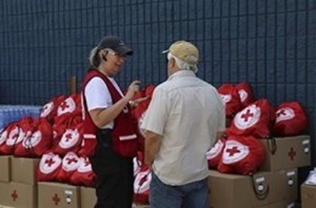 Une responsable de la Croix-Rouge discute avec un homme devant des boîtes et des trousses d'aide de la Croix-Rouge.