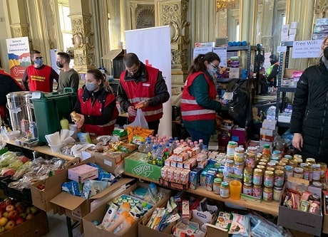 Des membres de la Croix-Rouge portant des masques derrière des tables remplies de nourriture et de fournitures.