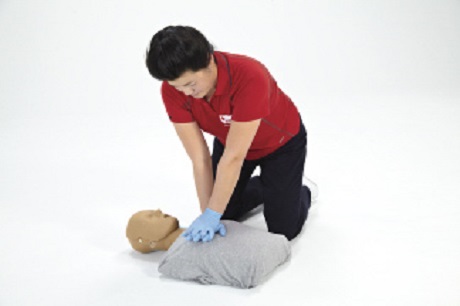 Une personne en chemise rouge effectuant des compressions thoraciques sur un mannequin.