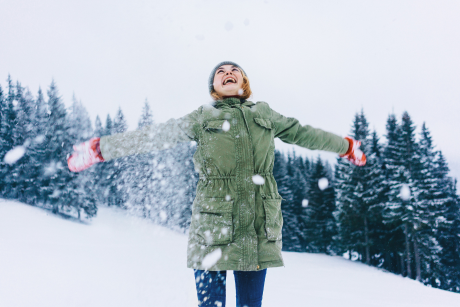 Une personne joyeuse se tient dans la neige, embrassant le paysage hivernal.