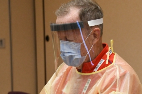 Un homme porte une visière, un masque et une blouse de protection contre la COVID-19.