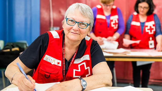 Une bénévole âgée de la Croix-Rouge sourit en remplissant des formalités administratives.