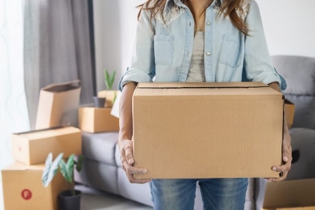 Une femme porte une boite de déménagement dans ses mains.