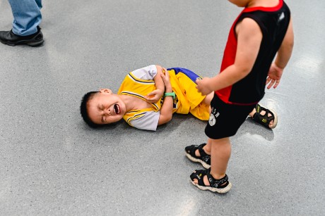 Un petit garçon habillé de linge de sport pleure au sol en se tenant le coude