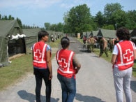Trois femmes bénévoles de la Croix-Rouge à l'extérieur, regardant une rangée de tentes de campement
