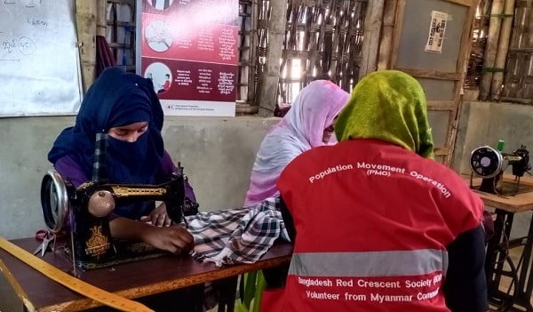 Femmes voilées qui apprennent à coudre autour d'une table avec une bénévole de la Croix-Rouge.
