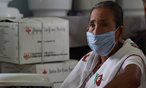 Une femme portant un masque médical, entourée de boîtes de la Croix-Rouge de l’Inde.
