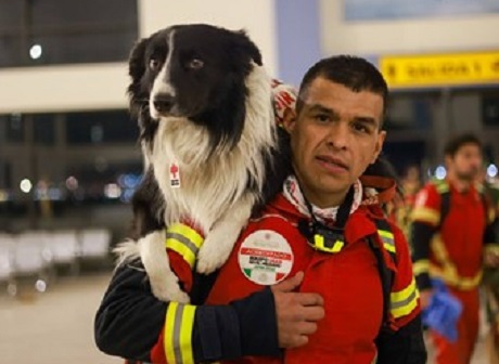 Un homme portant un uniforme rouge tient un chien sur son épaule
