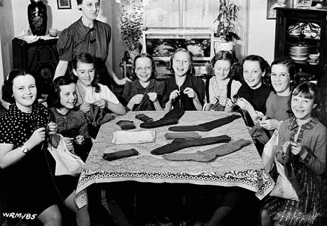 Un groupe de jeunes filles tricotent des vêtements en laine autour d’une table lors de la Seconde Guerre mondiale.