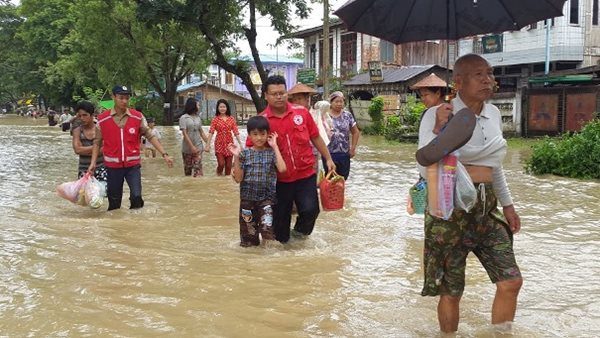 Des bénévoles Croix-Rouge accompagnant les sinistrés à travers un village inondé.