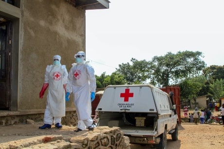 Deux hommes employés de la Croix-Rouge marchent dehors en habits de protection, puisqu'ils interviennent pour endiguer une nouvelle flambée d'Ebola en République démocratique du Congo.