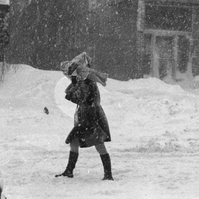 Une femme se promène de la rue en tenant un manteau pour se protéger de la neige.