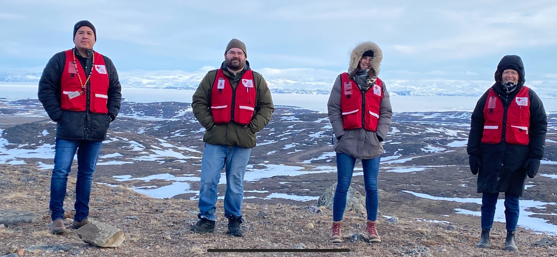Équipe de la Croix-Rouge portant des gilets rouges et des manteaux d'hiver, debout dans un paysage enneigé à Iqaluit.