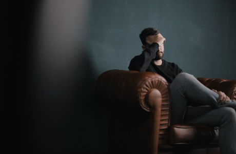 Un homme est assis sur un divan avec la main au front, déprimé.
