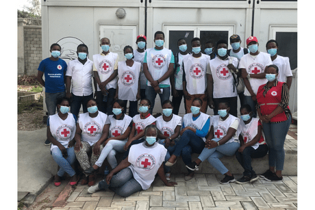 Un groupe de plusieurs personnes, portant un dossard blanc avec le logo de la Croix-Rouge et des masques, prennent la pose ensemble