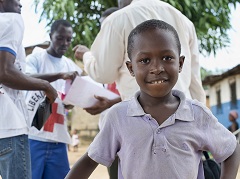 Derrière ce jeune garçon souriant, des bénévoles de la Croix-Rouge sensibilisent des habitants de Monrovia, au Libéria, aux dangers du virus Ebola.