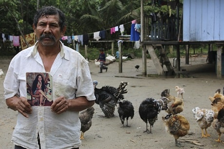 Un homme à l'apparence triste est entouré de poulets dans une cours arrière et montre une image d'une jeune femme (disparue) à la caméra.