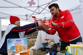 Deux membres de la Croix-Rouge se distribuent des boîtes de nourriture dans une tente blanche de la Croix-Rouge.