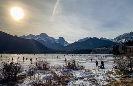 Des gens patinent sur un lac au bord des montagnes sous le soleil.