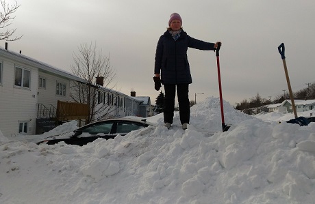 A woman standing on top of a small snow pile with shovel in hand