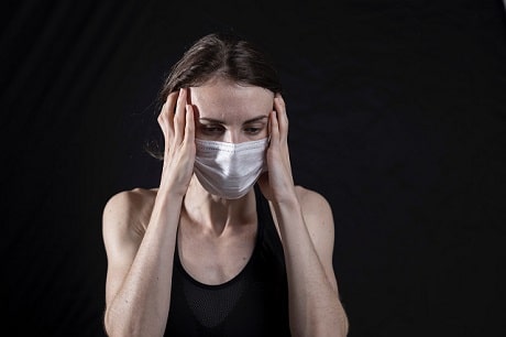 Une femme portant un masque au visage se tient le front avec les deux mains