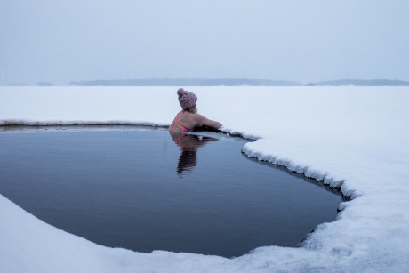 Une femme portant une tuque et un maillot de bain se baigne dans un lac gelé