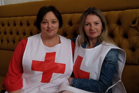 Deux femmes portant une veste de la Croix-Rouge sont assises ensemble sur un grand canapé brun.