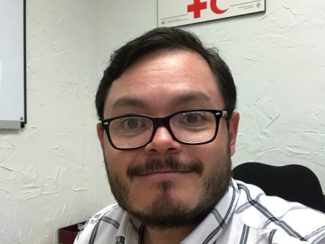 Juan, vêtu d'une chemise, de lunettes et souriant, est assis à son bureau de travail