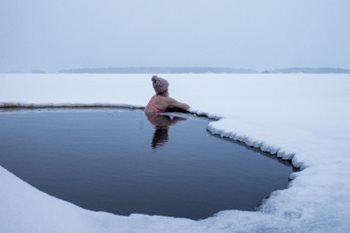 une femme portant un maillot de bain et une tuque se baigne dans un lac gelé