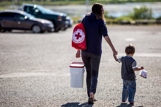 Une mère porte une trousse de soins de la Croix-Rouge canadienne tout en marchant et en tenant la main de son fils