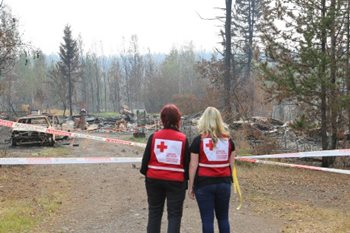 Deux femmes portent une veste de la Croix-Rouge et se trouvent devant de la dévastation