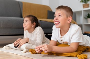 Une jeune fille et un jeune garçon regarde la télévision en riant