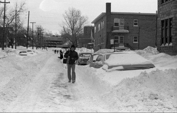 Un homme marche dans les rues enneigées aux côtés de voitures ensevelies sous la neige.