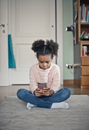 Une jeune fille est assise au sol et regarde un téléphone portable en semblant triste